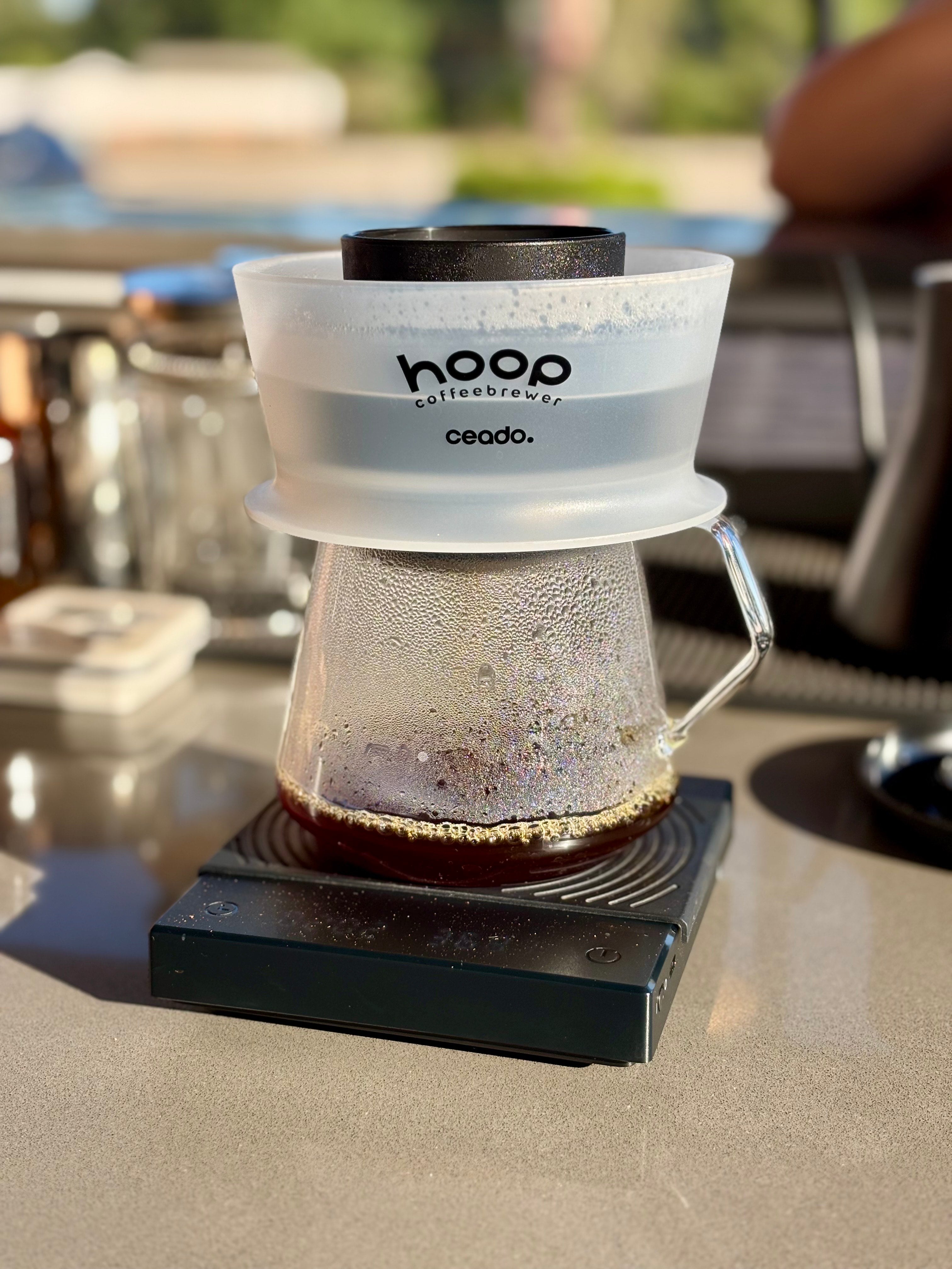 A stylish hoop coffee brewer resting on a table with a cup of coffee, highlighting a perfect brewing setup.