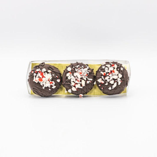 A trio of chocolate-covered cookies displayed on a white surface, showcasing dark chocolate peppermint Oreos in a gift box