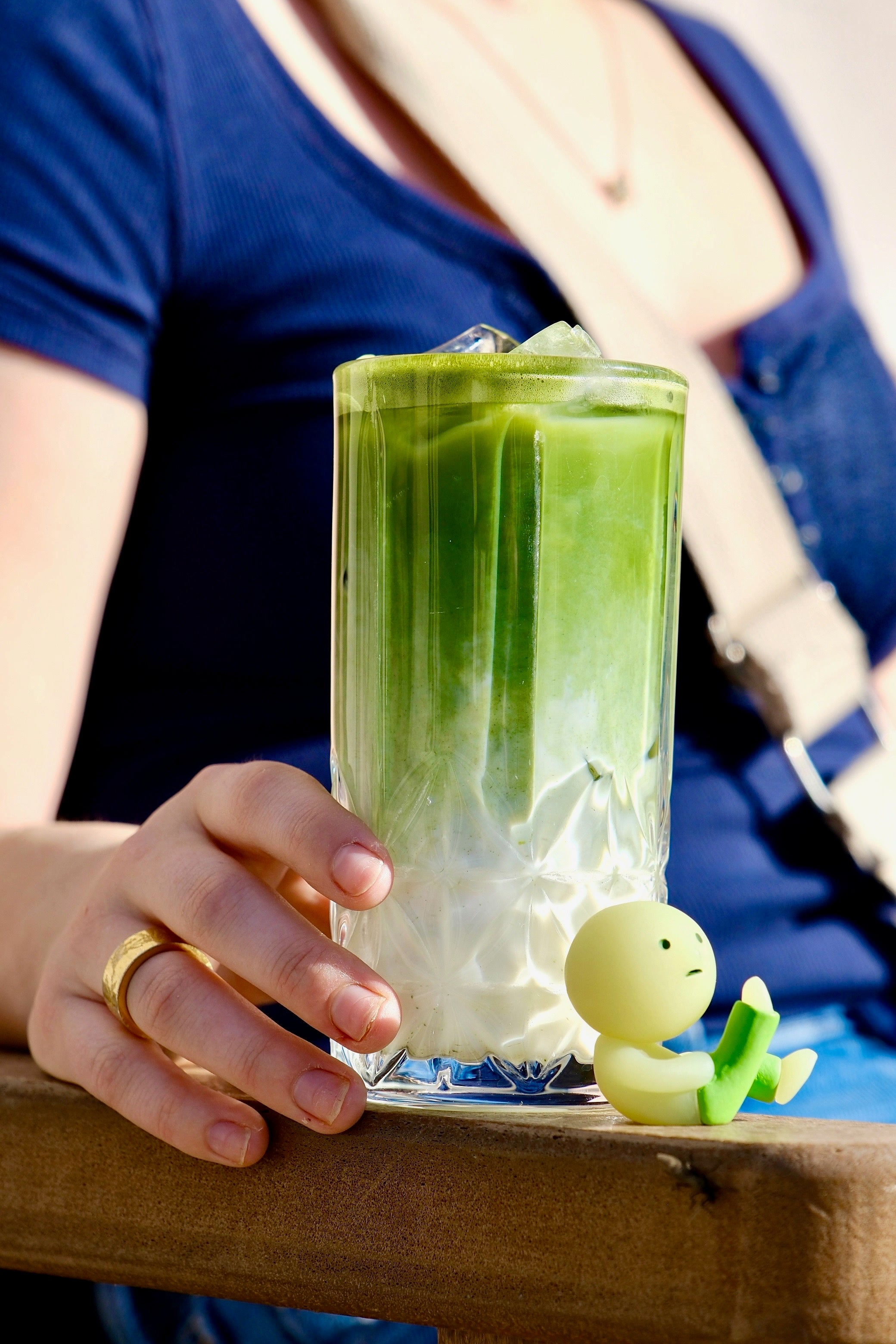 Person holding an iced matcha latte with a toy in the foreground.
