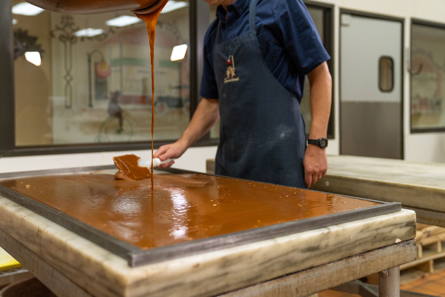 Person pouring caramel onto a marble table in a kitchen setting.