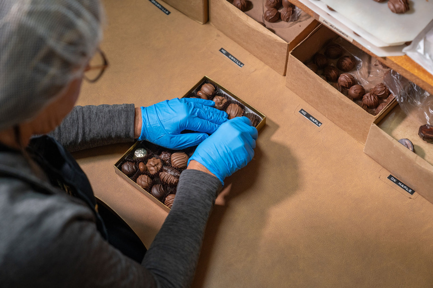 Person packaging chocolates into boxes with gloves on a wooden table.