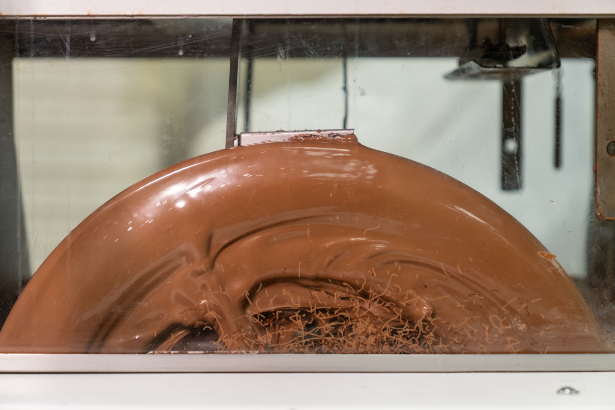 Chocolate being processed in a machine with a reflective surface.