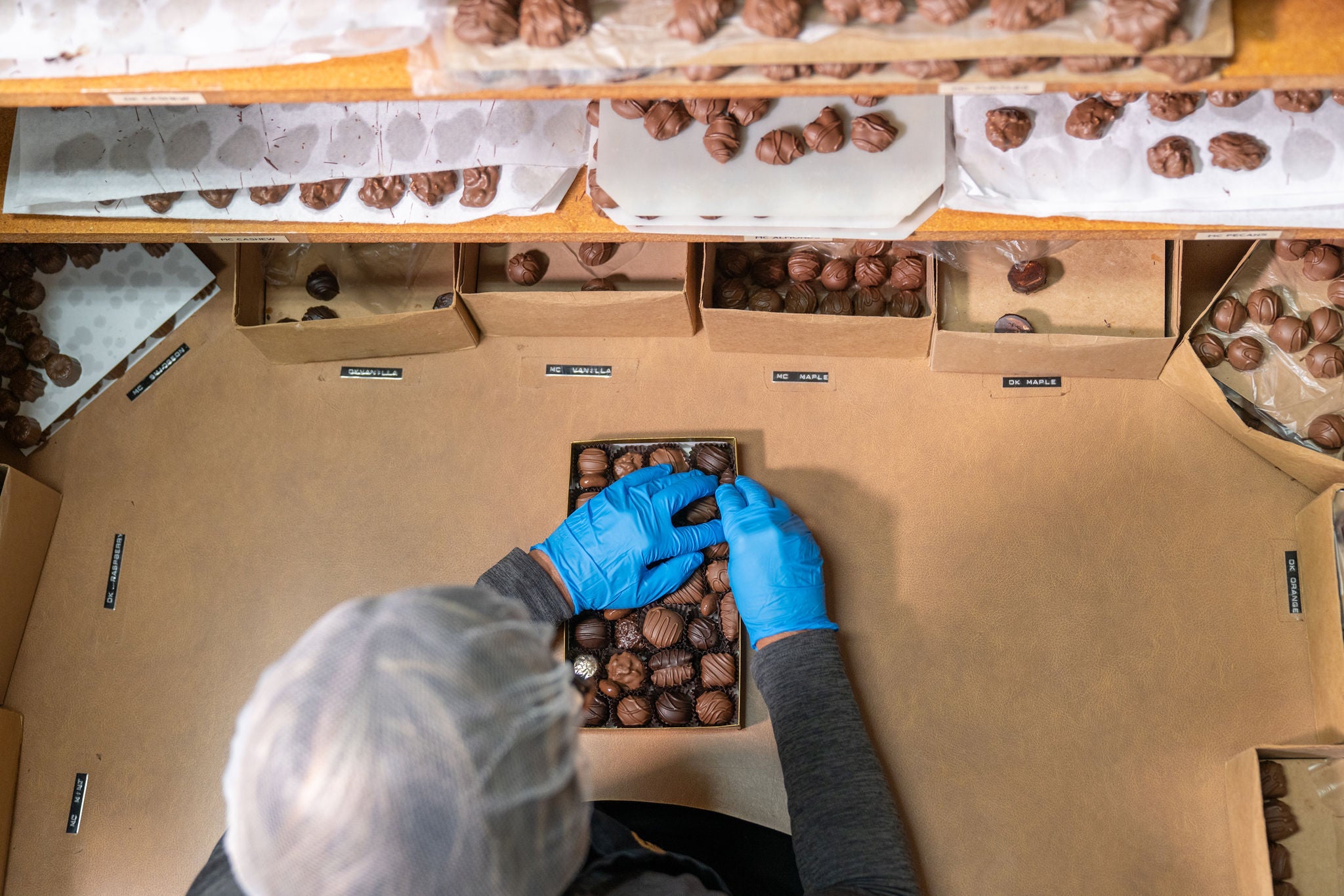 Person packaging truffles into boxes with gloves on, surrounded by more boxes and truffles.