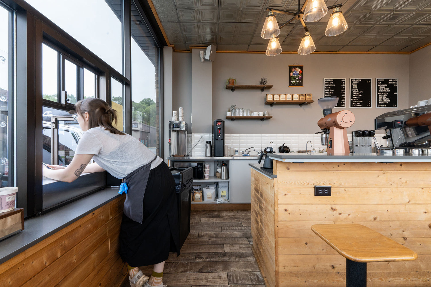 Person working inside a modern coffee shop with wooden counter and large windows. Serving Morningsong Coffee Roasters.